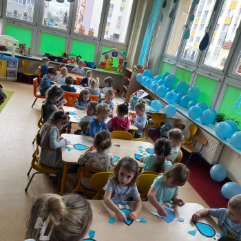 Dzieci wykonują prace plastyczne na wyciętych kropelkach wody, w tle widzimy niebieskie balony