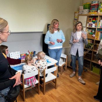 Stolik przy ścianie, siedzi przy nim dwójka dzieci, obok stolika stoją dwie panie