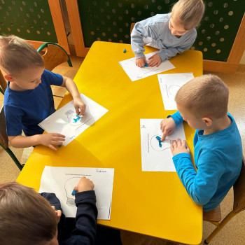 Grupa dzieci siedząca przy stolikach malująca obrazki